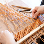 Artisan hands weaving natural rattan using traditional 
wooden frame — handcrafted basket making process