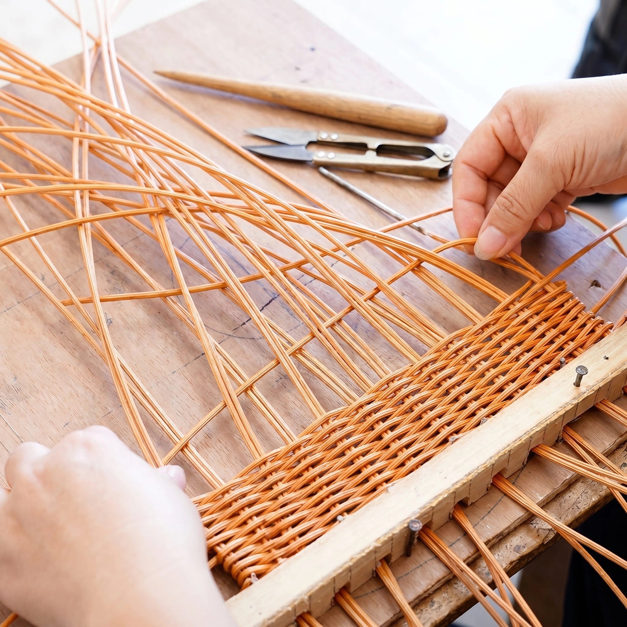Artisan hands weaving natural rattan using traditional 
wooden frame — handcrafted basket making process