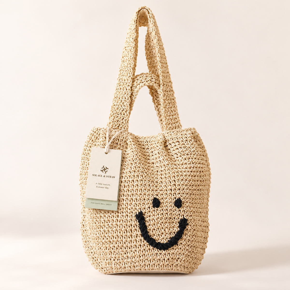 Smiley Woven Shoulder Bag in beige with a black smiley face, front view with a Solace & Straw hangtag