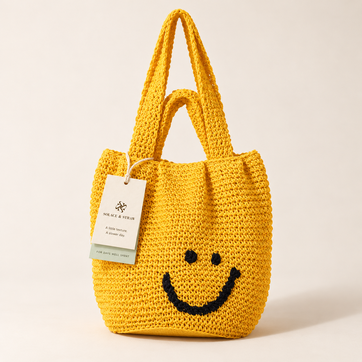 Smiley Woven Shoulder Bag in yellow with a black smiley face, front view with a Solace & Straw hangtag
