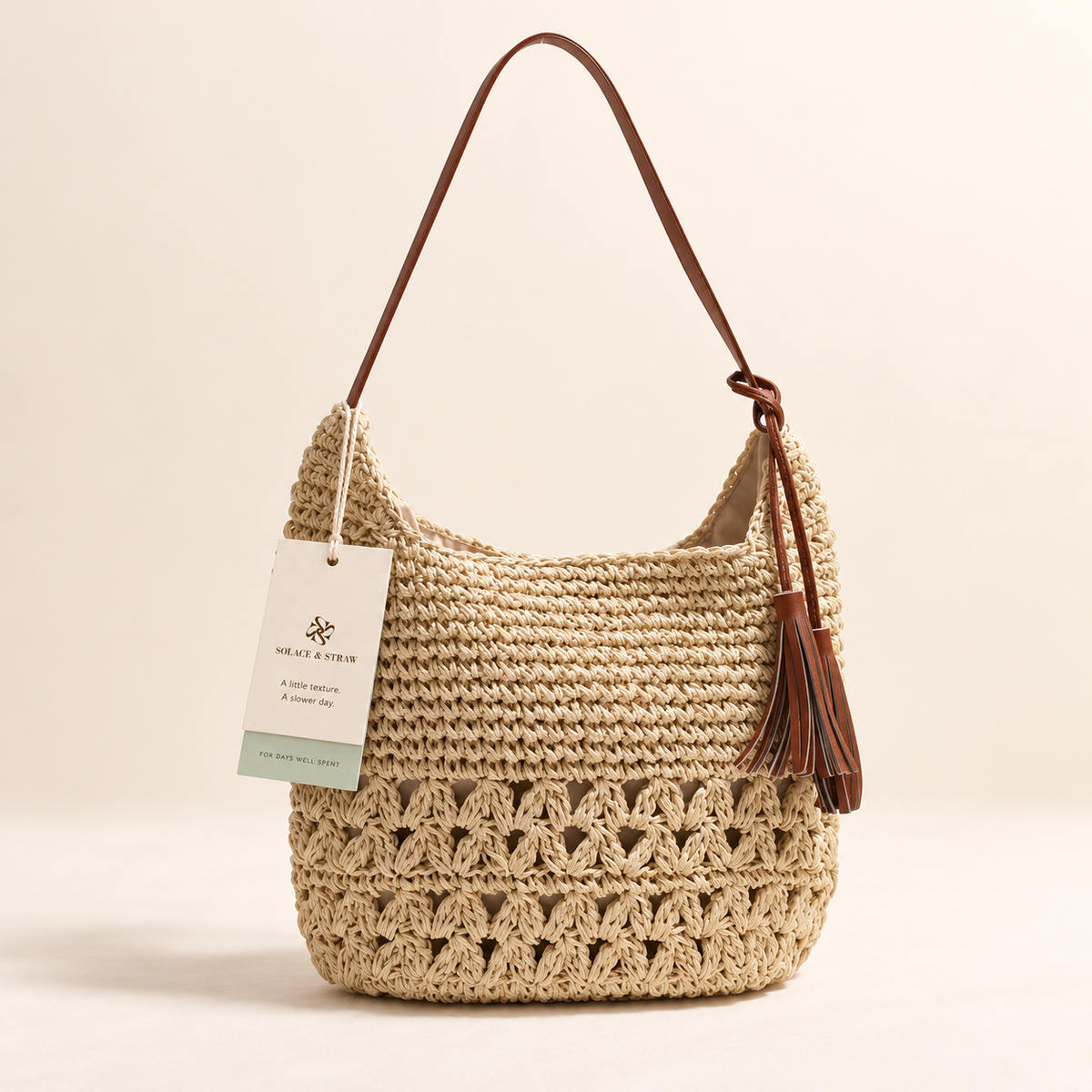 Heart Tassel Shoulder Bag in beige with openwork crochet and a side tassel, front view with a Solace & Straw hangtag