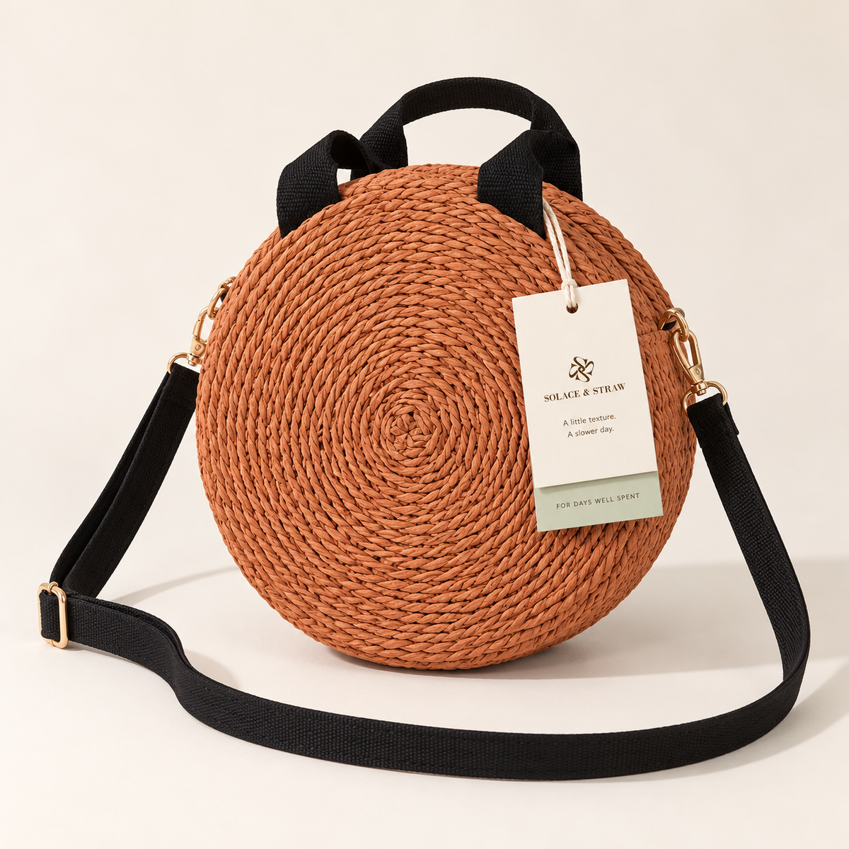 Round Woven Crossbody in terracotta orange with black straps, front view with a Solace & Straw hangtag