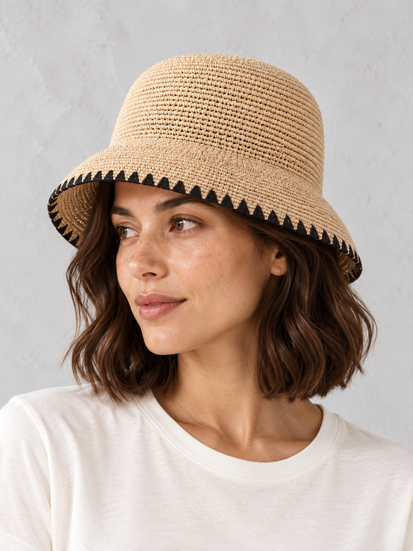 Woman wearing the natural Black Trim Straw Hat with black triangular edging beside a pale wall